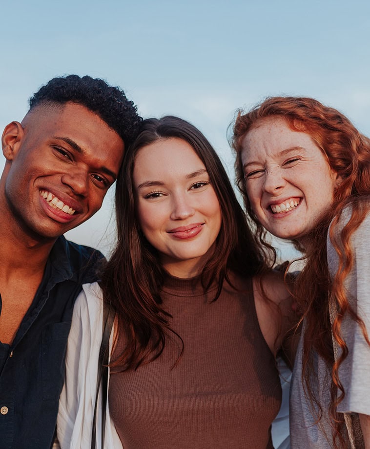 A man and two women smiling and posing for a photo with a blue sky behind